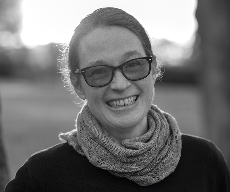 Angela smiling widely. She is a white person wearing large glasses with her hair pulled back.